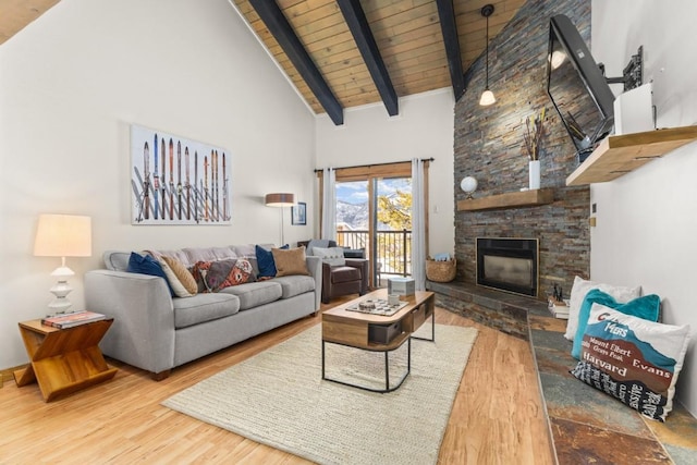 living room featuring high vaulted ceiling, beamed ceiling, a stone fireplace, and wood finished floors