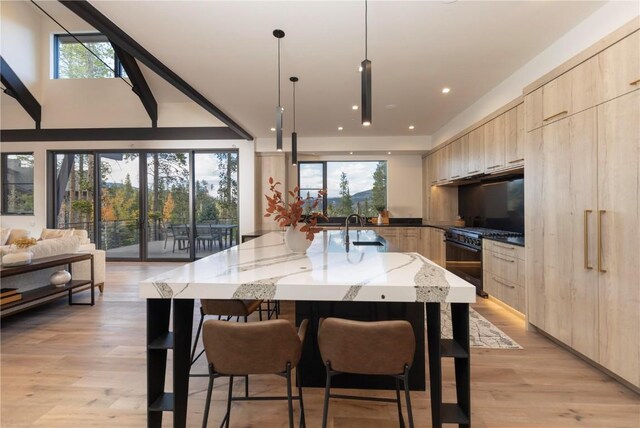 kitchen with black gas range, light stone counters, light brown cabinets, and hanging light fixtures