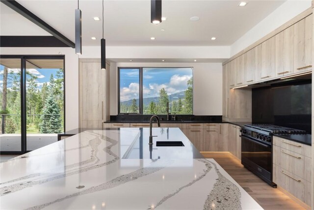 kitchen featuring light stone counters, light brown cabinets, pendant lighting, and black gas range oven