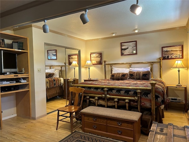 bedroom featuring a closet, light hardwood / wood-style flooring, track lighting, and ornamental molding