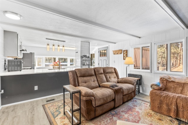 living area featuring a textured ceiling, visible vents, beam ceiling, and wood finished floors