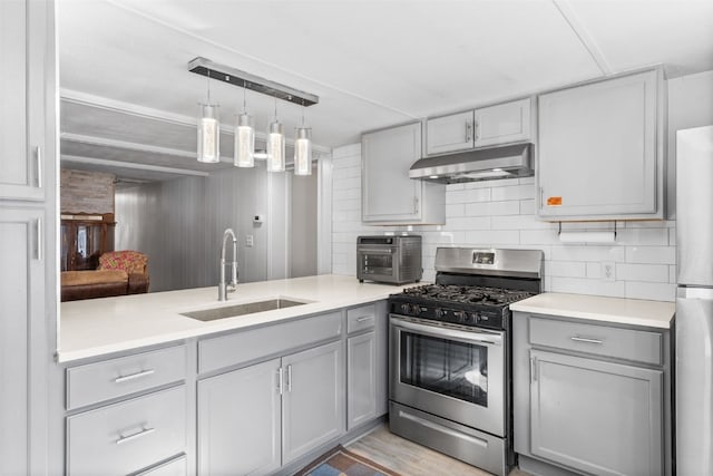 kitchen with gray cabinetry, appliances with stainless steel finishes, a sink, and under cabinet range hood