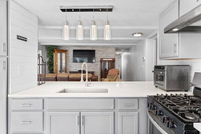 kitchen with a peninsula, light countertops, under cabinet range hood, stainless steel range with gas cooktop, and a sink