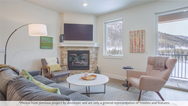 living room featuring ceiling fan, light hardwood / wood-style floors, and a stone fireplace