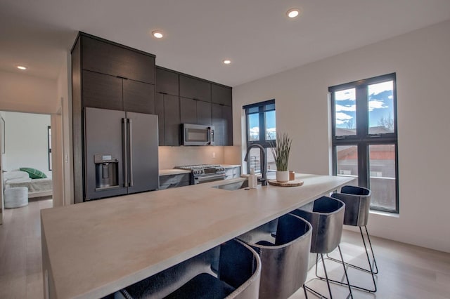 kitchen with appliances with stainless steel finishes, a kitchen island with sink, sink, and a breakfast bar area