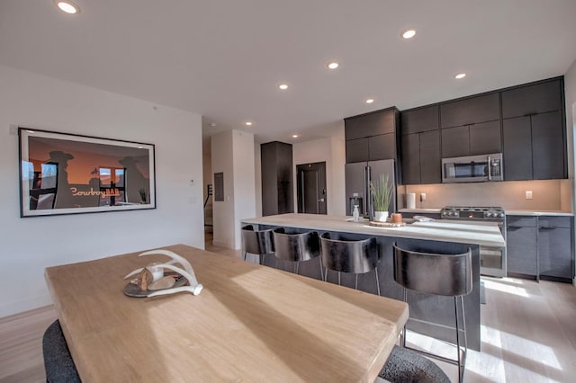 kitchen with light wood-type flooring, a kitchen breakfast bar, an island with sink, and appliances with stainless steel finishes