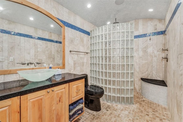 bathroom featuring a tile shower, tile walls, vanity, and toilet