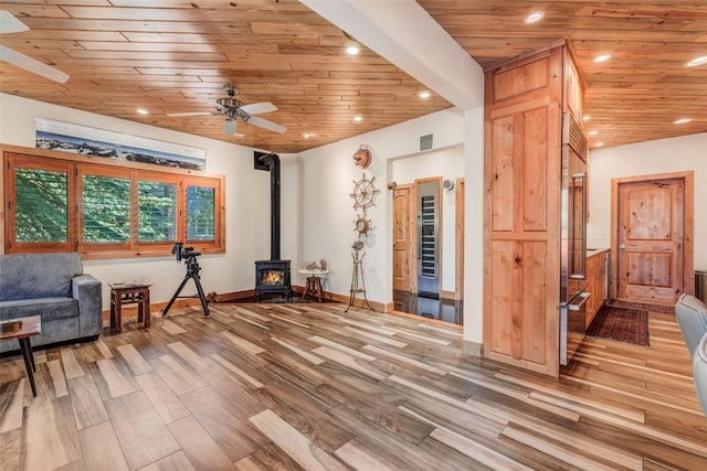 sitting room with wood ceiling, light wood-type flooring, ceiling fan, and a wood stove