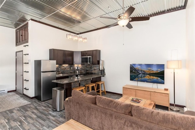 living room with dark hardwood / wood-style flooring, a towering ceiling, ceiling fan, and a baseboard heating unit