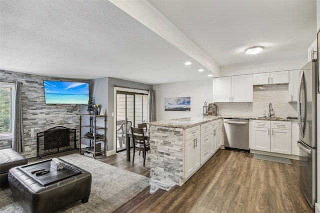 kitchen with white cabinets, dark hardwood / wood-style floors, appliances with stainless steel finishes, light stone counters, and kitchen peninsula