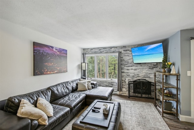 living room featuring a stone fireplace, wood-type flooring, and a textured ceiling