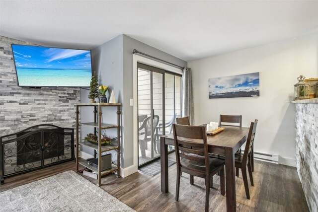 dining space with a stone fireplace, dark hardwood / wood-style flooring, and a baseboard heating unit