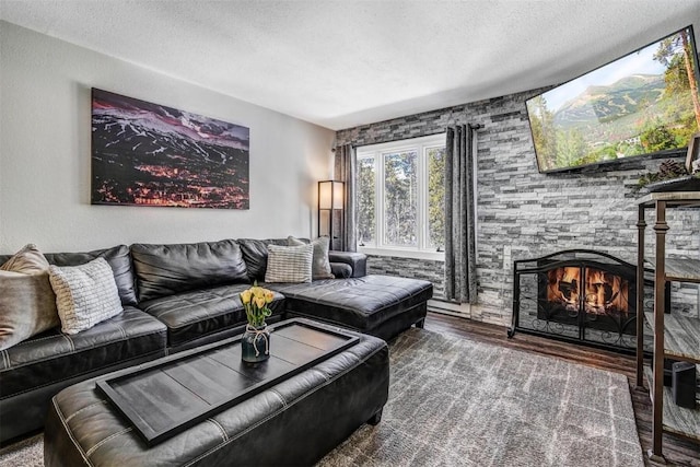 living room featuring a textured ceiling, hardwood / wood-style flooring, and a stone fireplace