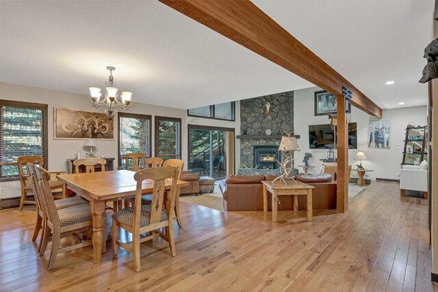 dining room featuring beamed ceiling, a chandelier, a fireplace, and light hardwood / wood-style flooring