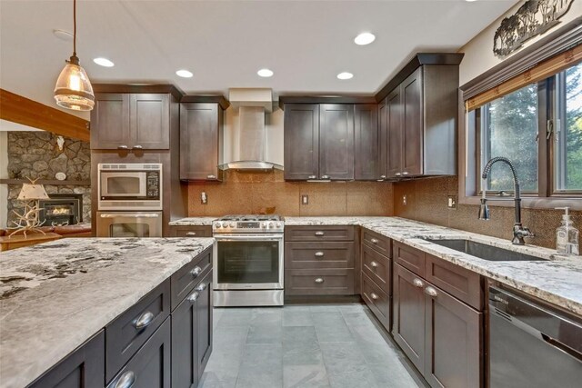 kitchen featuring wall chimney range hood, sink, decorative light fixtures, dark brown cabinets, and stainless steel appliances