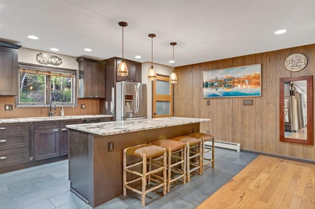 kitchen featuring pendant lighting, a center island, sink, wooden walls, and stainless steel fridge with ice dispenser