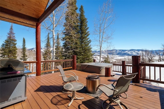 snow covered deck featuring a mountain view, a hot tub, and a grill