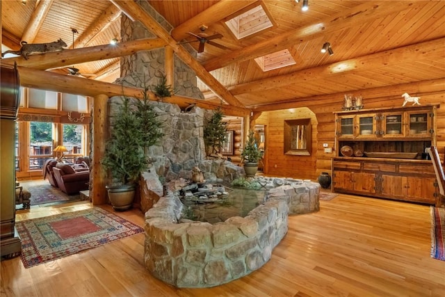 living room featuring a skylight, high vaulted ceiling, log walls, beamed ceiling, and light wood-type flooring