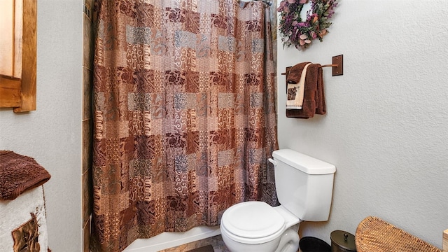 full bath featuring a shower with shower curtain, a textured wall, and toilet