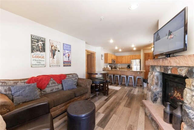 living room with light hardwood / wood-style floors, a stone fireplace, and sink