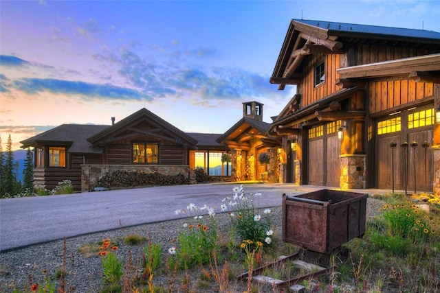 back of house at dusk with a garage, stone siding, board and batten siding, and driveway