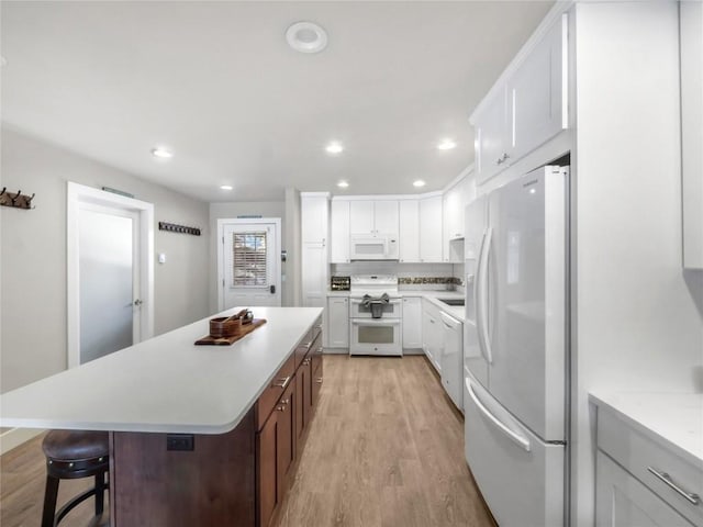 kitchen featuring a kitchen breakfast bar, light hardwood / wood-style flooring, white cabinetry, white appliances, and a kitchen island