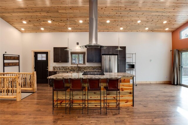 kitchen featuring appliances with stainless steel finishes, light stone counters, island range hood, a high ceiling, and a kitchen island