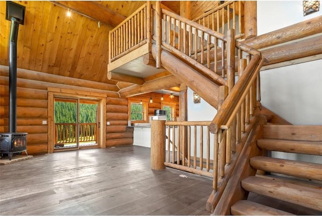 stairway featuring a high ceiling, rustic walls, a wood stove, and wood-type flooring