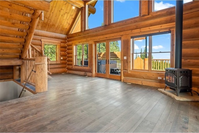 unfurnished living room featuring hardwood / wood-style floors, a wood stove, high vaulted ceiling, rustic walls, and beamed ceiling