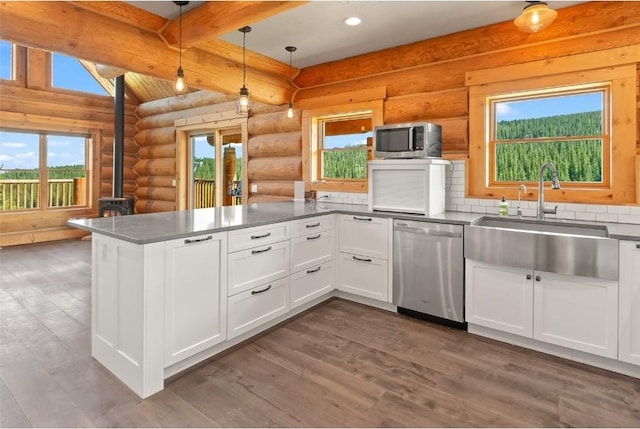 kitchen with kitchen peninsula, stainless steel appliances, sink, log walls, and white cabinetry