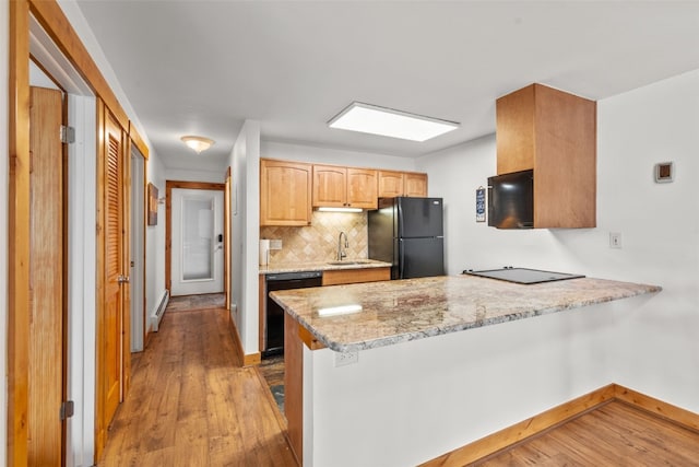 kitchen featuring light stone counters, backsplash, kitchen peninsula, black appliances, and hardwood / wood-style flooring