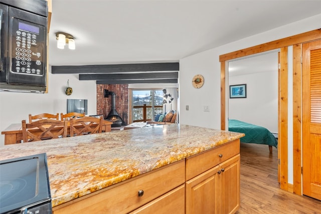 kitchen featuring light wood-type flooring, light stone counters, beam ceiling, range, and a wood stove