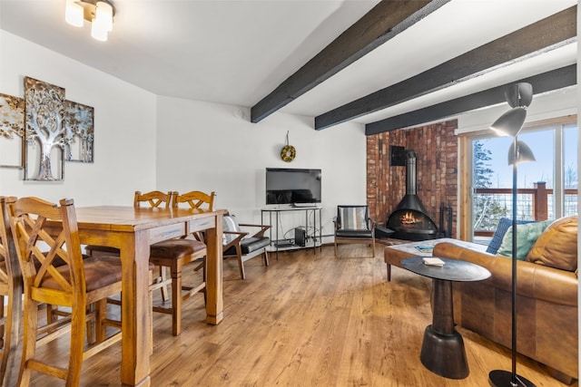 interior space with beam ceiling, a wood stove, and light wood-type flooring