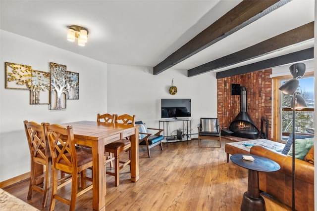 dining area with beam ceiling, a wood stove, and hardwood / wood-style floors