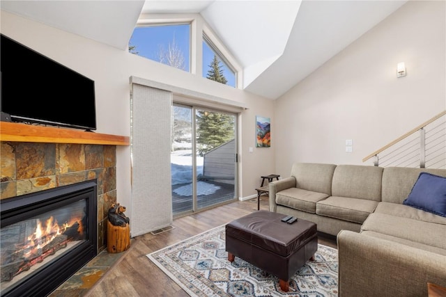 living room with wood-type flooring, a tiled fireplace, and high vaulted ceiling