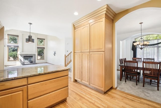 kitchen featuring light brown cabinetry, pendant lighting, stone countertops, a notable chandelier, and a tiled fireplace