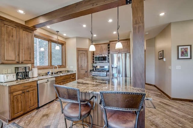 kitchen featuring pendant lighting, light hardwood / wood-style flooring, appliances with stainless steel finishes, a kitchen island, and light stone counters