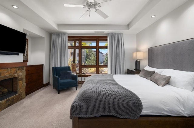 bedroom with a fireplace, light colored carpet, a raised ceiling, and ceiling fan