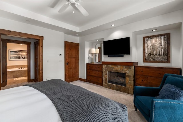 carpeted bedroom with ensuite bathroom, a stone fireplace, and ceiling fan