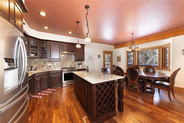 kitchen featuring hanging light fixtures, an island with sink, tasteful backsplash, dark brown cabinets, and stainless steel appliances