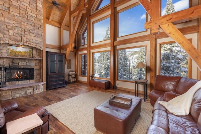 living room with beamed ceiling, wood-type flooring, high vaulted ceiling, and a stone fireplace