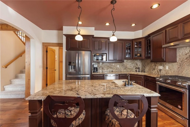 kitchen with decorative backsplash, dark brown cabinets, an island with sink, and appliances with stainless steel finishes