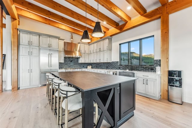 kitchen with appliances with stainless steel finishes, beamed ceiling, a kitchen island, hanging light fixtures, and range hood