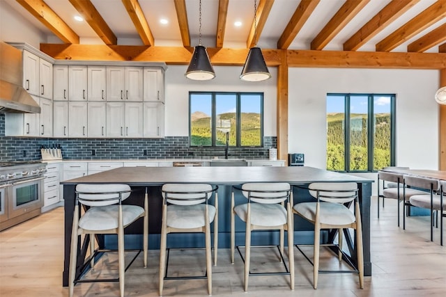 kitchen with range with two ovens, sink, hanging light fixtures, tasteful backsplash, and white cabinetry