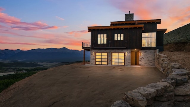 back house at dusk with a mountain view, a garage, and a balcony