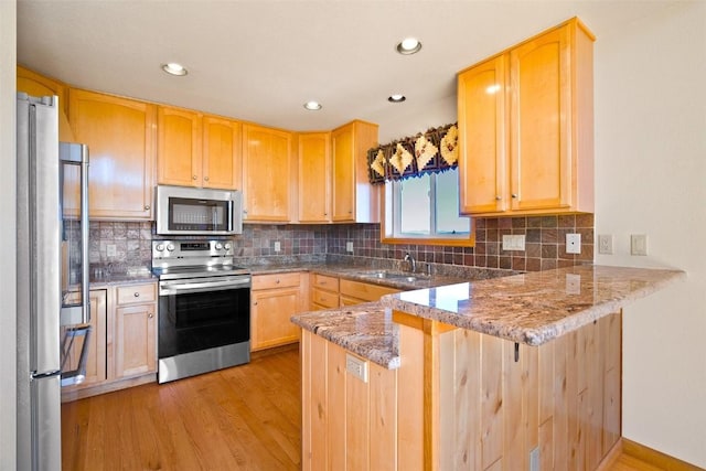 kitchen featuring kitchen peninsula, stainless steel appliances, light stone counters, and sink