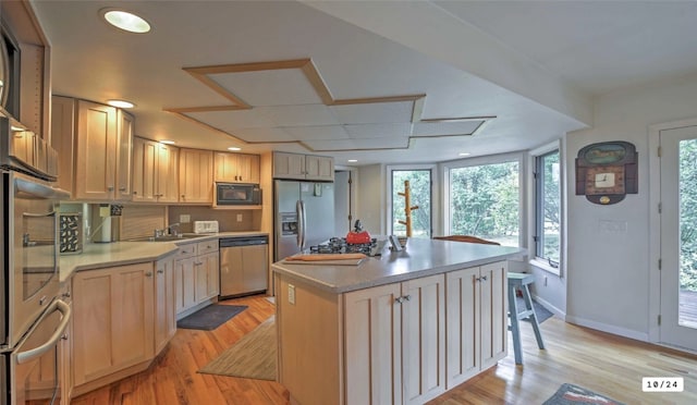 kitchen featuring a center island, stainless steel appliances, light wood-style floors, light countertops, and baseboards