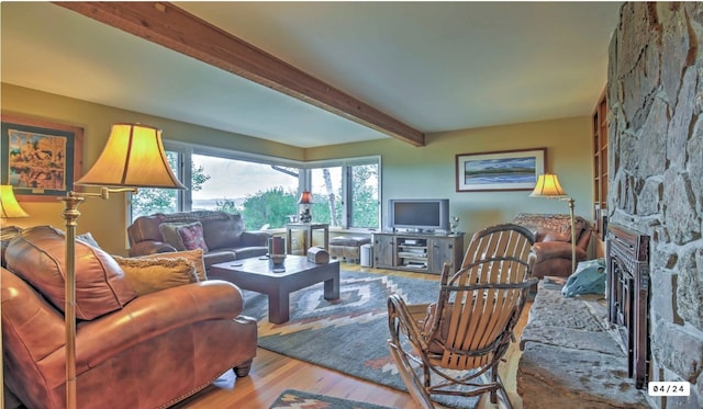 living room featuring beamed ceiling, a stone fireplace, and wood finished floors