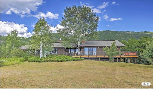 rear view of house with a deck with mountain view and a lawn