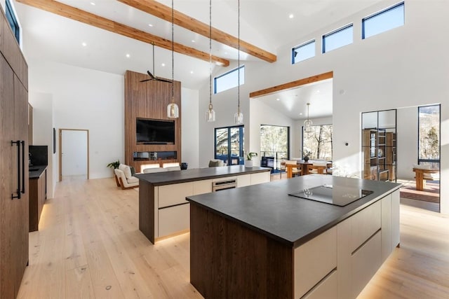 kitchen with a high ceiling, beamed ceiling, black electric stovetop, a kitchen island, and light wood-type flooring